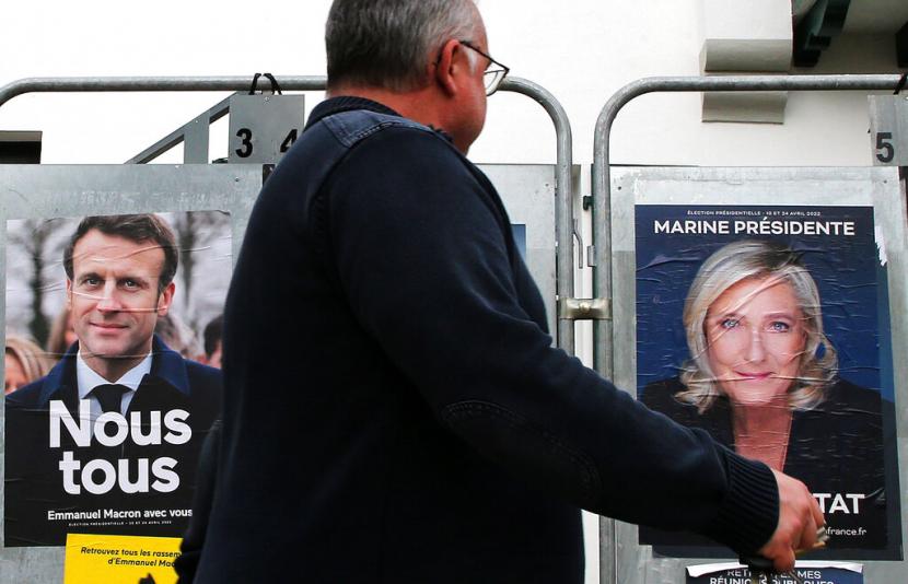Seorang pria berjalan melewati poster kampanye presiden dari Presiden Prancis dan kandidat tengah untuk pemilihan kembali Emmanuel Macron dan kandidat presiden sayap kanan Prancis Marine Le Pen di Anglet barat daya Prancis Rabu 8 April 2022