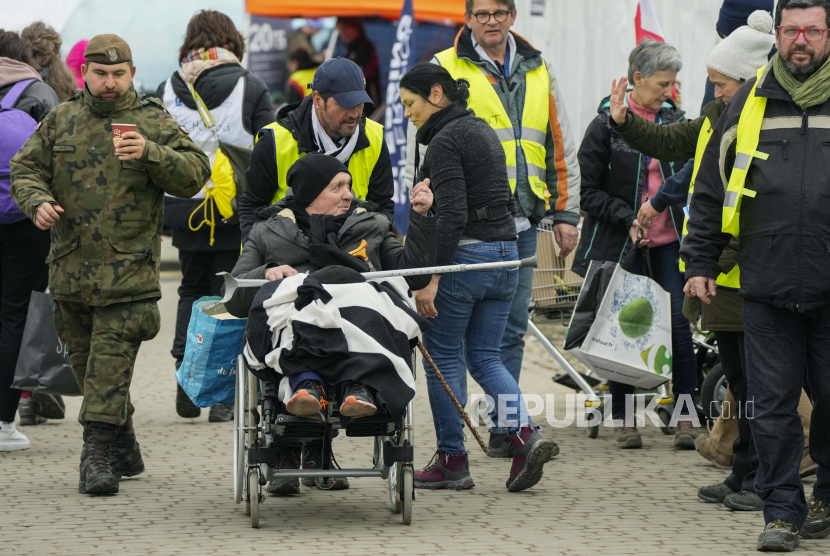 Relawan membantu seorang pengungsi di kursi roda setelah melarikan diri dari perang dari negara tetangga Ukraina di perbatasan di Medyka Polandia tenggara Rabu 6 April 2022