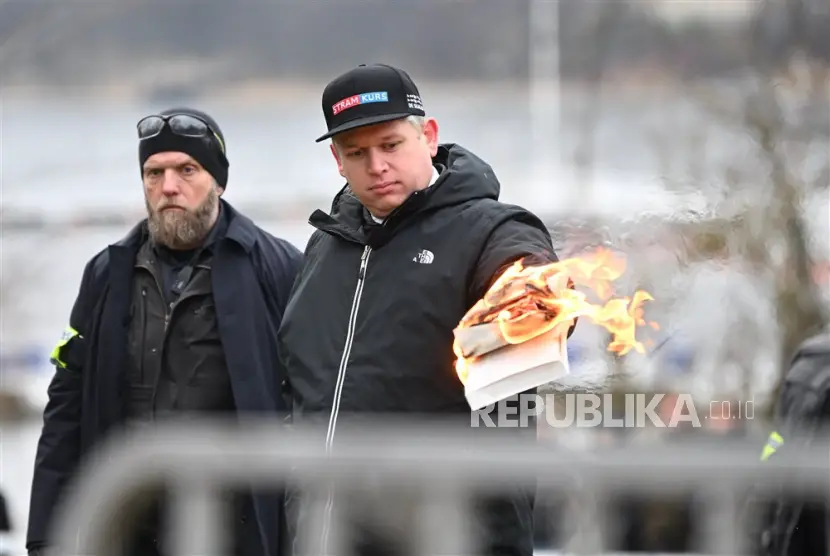 Pemimpin partai politik sayap kanan Denmark Stram Kurs Rasmus Paludan membakar salinan Alquran sambil diawasi oleh petugas polisi saat dia melakukan protes di luar kedutaan Turki di Stockholm Swedia 21 Januari 2023