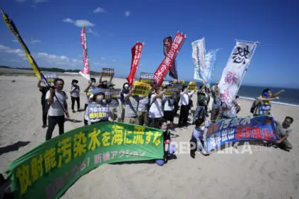 Orang-orang melakukan protes membawa spanduk bertuliskan  bertuliskan: Menolak pembuangan Limbah air radioaktif yang telah diolah ke laut di pantai menuju pembangkit listrik tenaga nuklir Fukushima Daiichi, yang rusak akibat gempa bumi dan tsunami besar pada 11 Maret 2011, di kota Namie, timur laut Jepang, Kamis, (24/8/2023).